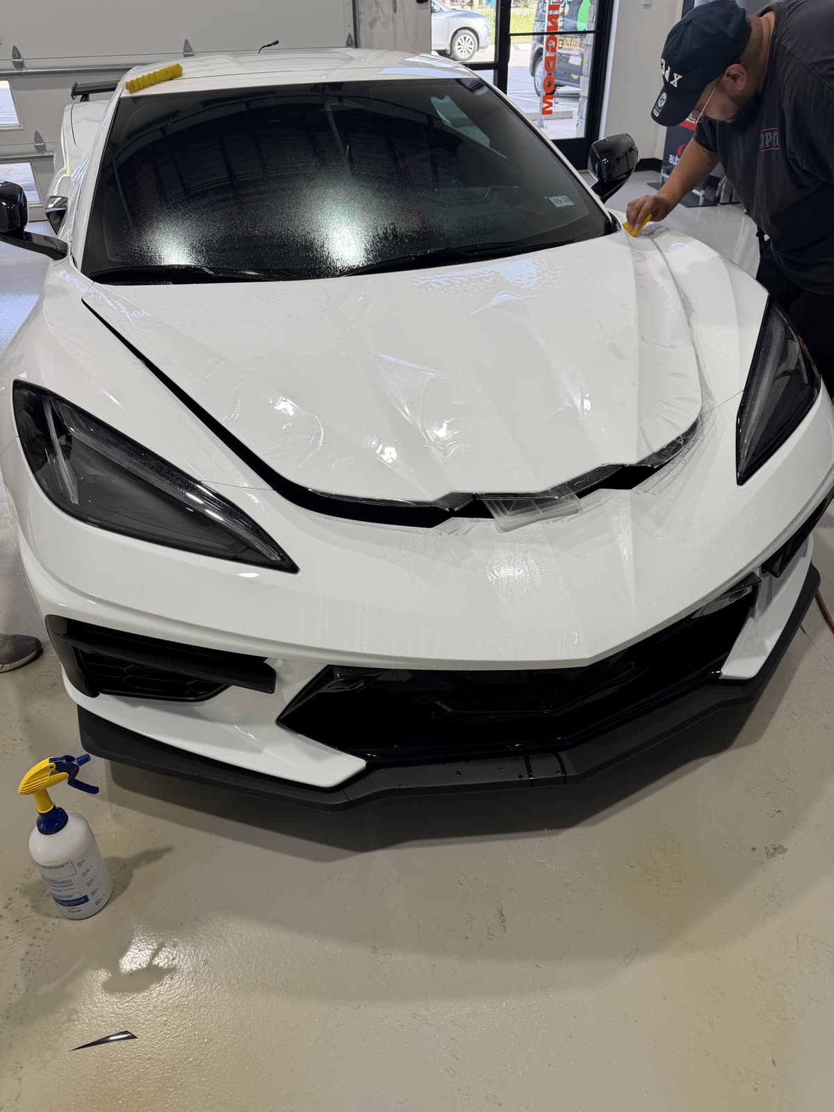 Installer fitting full front PPF on the hood and bumper of a white C8 Corvette